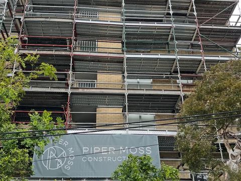 Scaffold with blue mesh on a brick apartment block, under a Piper Moss Constructions banner